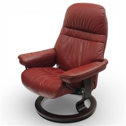Ekornes - Stressless reclining armchair and matching footstool, upholstered in oxblood leather with padded headrest and segmented back cushion, shaped armrests with exposed adjustment handles, raised on stained laminated beech circular swivel base, the conforming stool on matching ring base