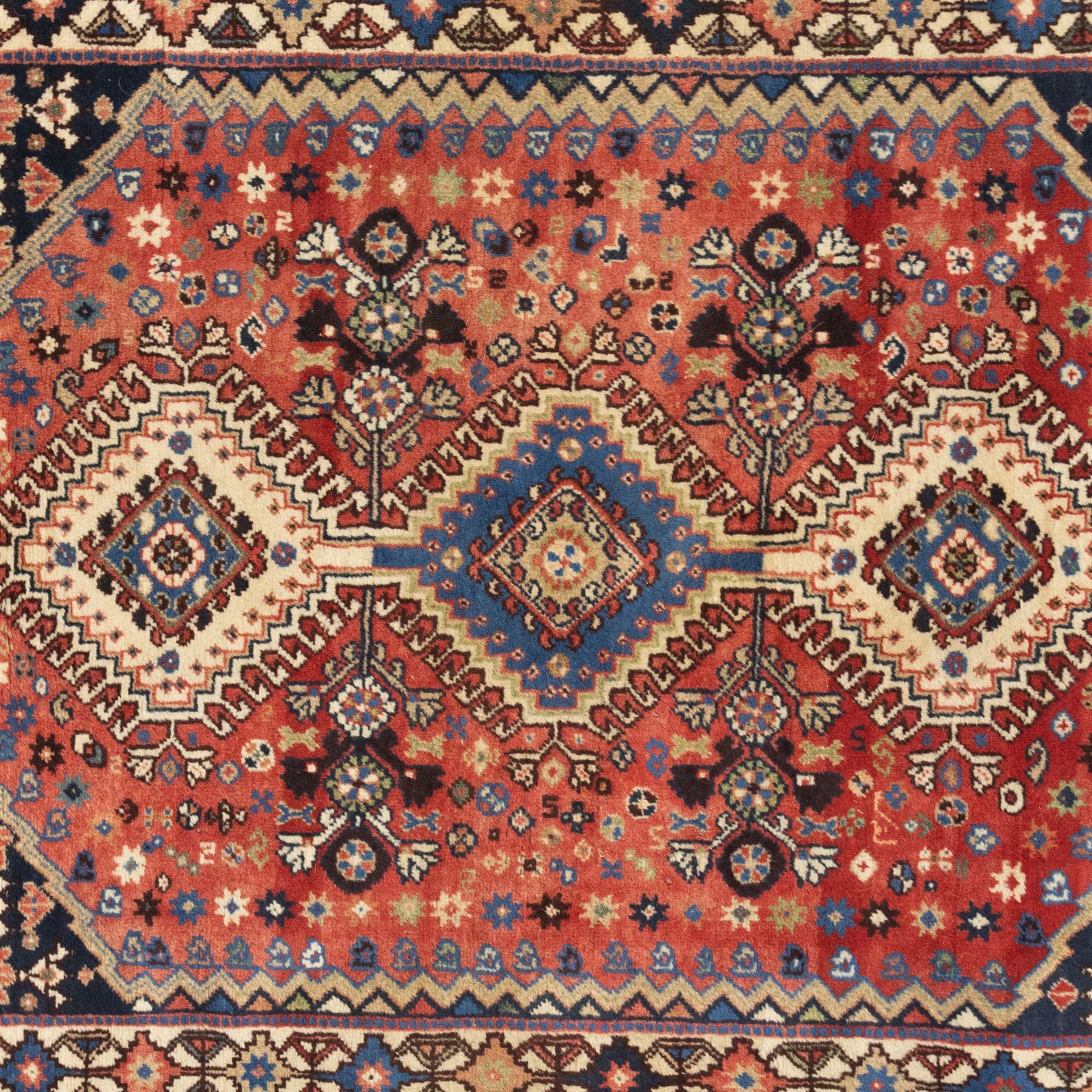 Persian Shiraz rug, wool on cotton foundation, with central row of linked diamond medallions in ivory, indigo and madder tones, stylised rosettes and angular vine motifs throughout, framed by a geometric border