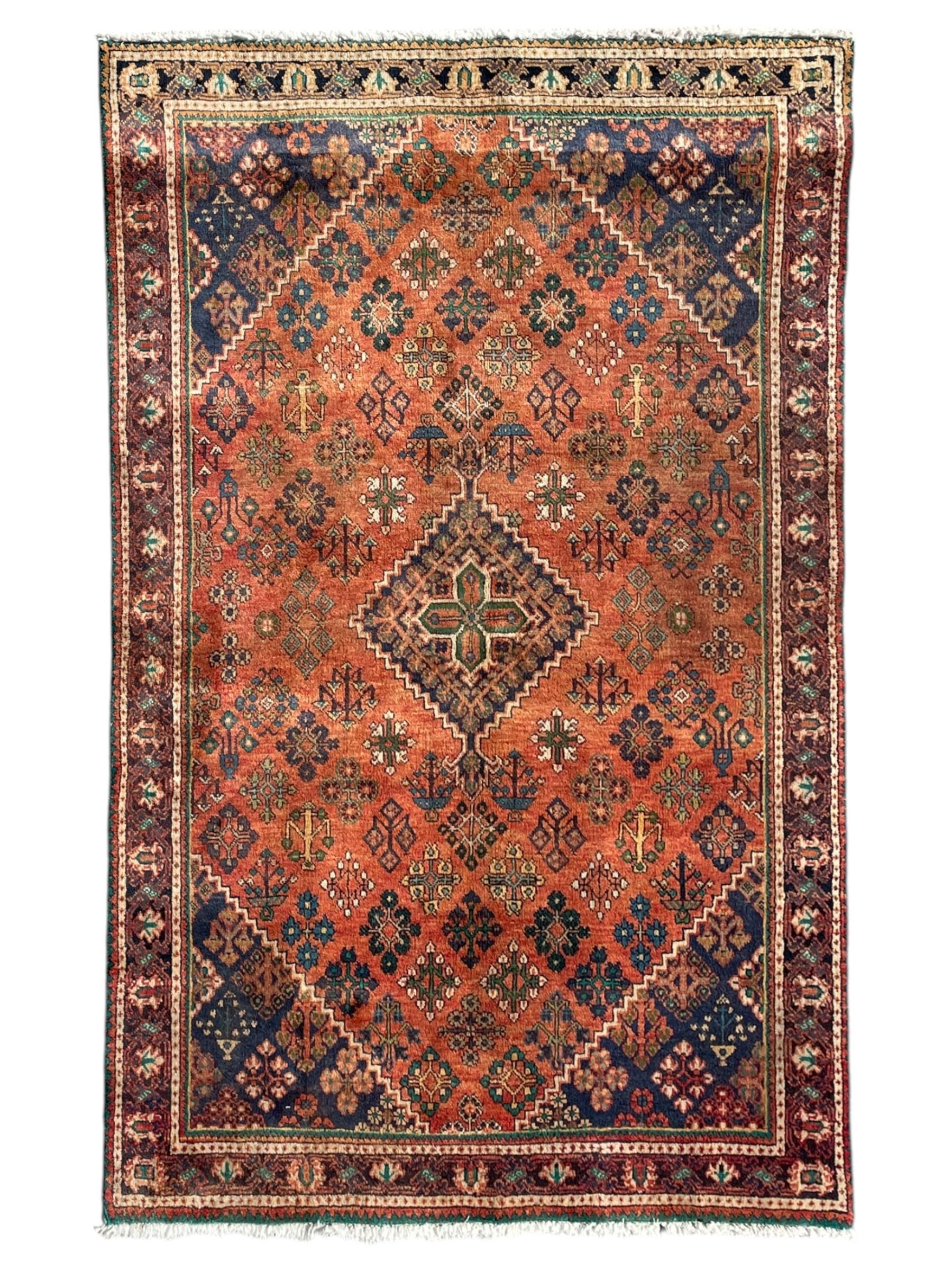 Persian Joshaghan rust ground rug, stepped lozenge medallion surrounded by repeating foliate lozenge motifs, the border decorated with stylised plant motifs, within geometric guard stripes
