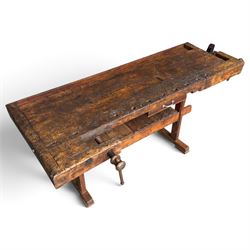 Large early 20th century rustic stained reclaimed pine workbench, the substantial plank top with recessed tool well and two homemade wooden screw vices, above a single frieze drawer and slatted undertier, raised on trestle end supports