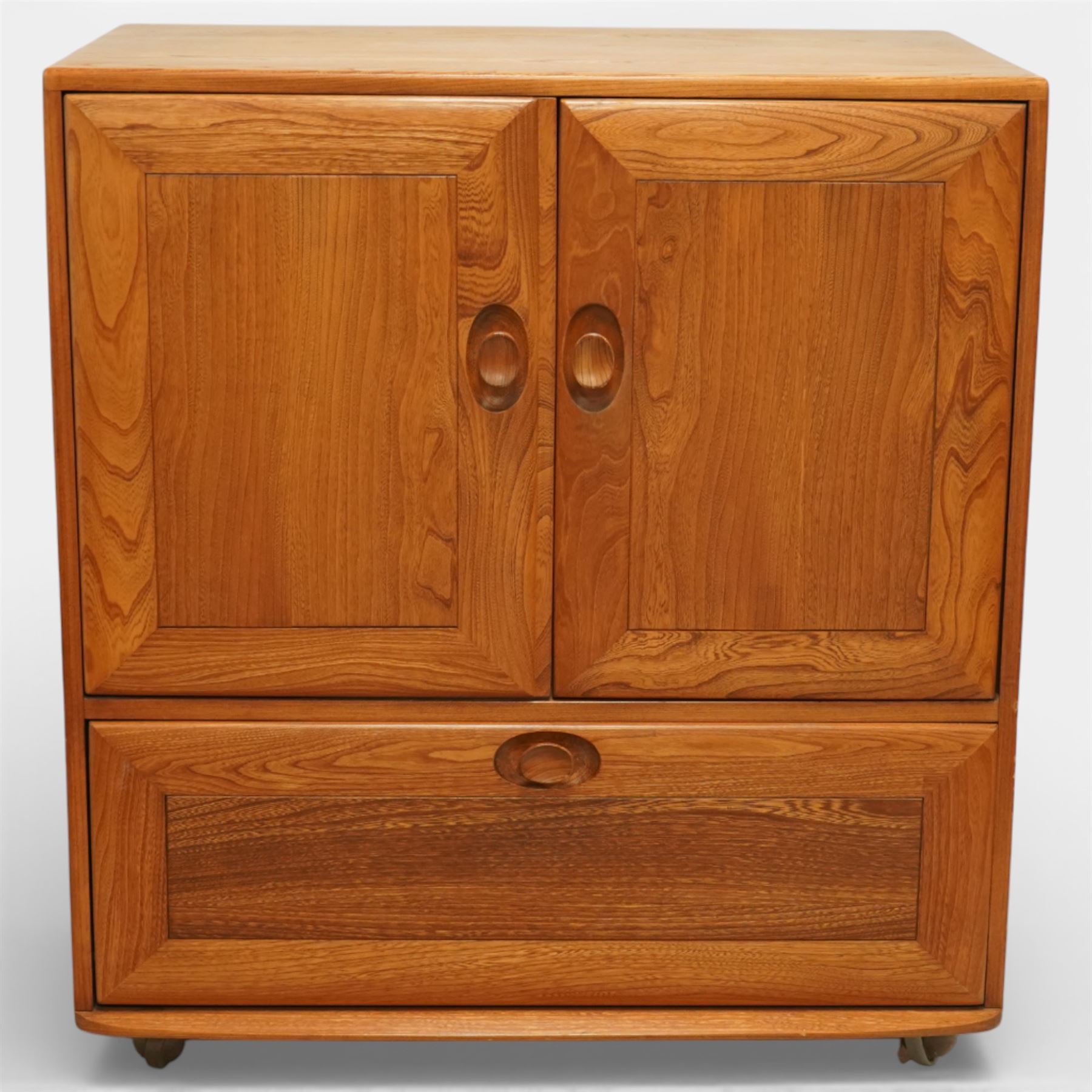 Ercol - elm television cabinet, rectangular top with chamfered edges, fitted with a pair of fielded panel cupboard doors with recessed oval pulls, opening to reveal an adjustable shelf and open back for cables, the lower section with drop-front compartment fitted with record slots and wire dividers, raised on concealed castors