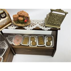 Collection of miniature dolls house grocery shop furniture and produce, comprising glazed corner counter with brass style cash register, shelved preserves unit, pies, cheese board and trays of meats, pair of white cheese counters, biscuit display with six tins, glazed preserves cabinet, pair of shop chairs and four further cheese boards complete with grapes and label flags