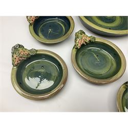 Studio pottery terracotta dishes, comprising large serving dish and seven smaller dishes, each with moulded fish to rim, upon a blue green glaze by Josie Walter, signed beneath, largest D31cm