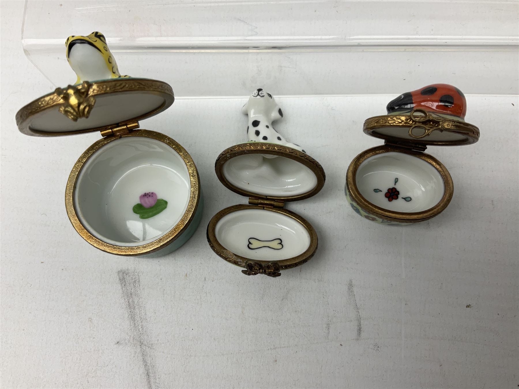 Group of Limoges trinket boxes, to include a number of novelty examples, including examples modelled as Noah's ark, shotgun case containing shotguns, picnic basket containing food, toad reading book seated upon a lily pad, etc., (9)