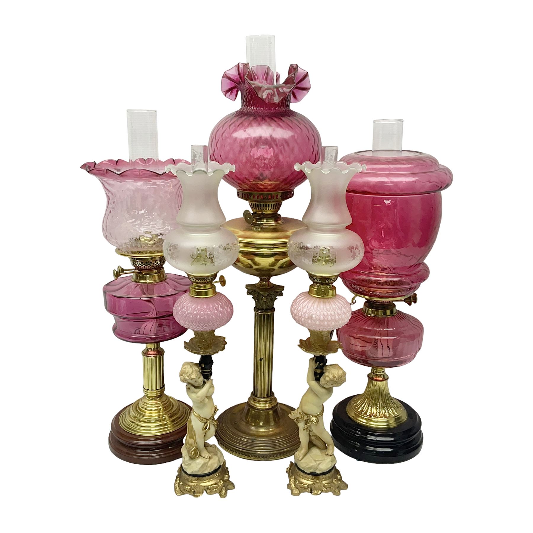 Victorian cast brass oil lamp, with fluted pink glass shade, together with two smaller brass oil lamps with pink shades and reservoirs and a pair of oil lamps, the bases modelled as putti, with pink glass reservoir  and frosted shades, tallest H70cm
