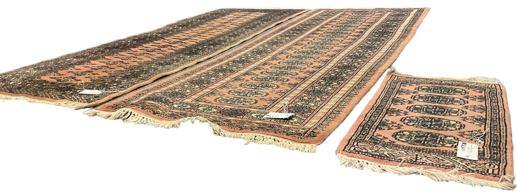 Bokhara peach ground runner, decorated with a single row of Gul motifs (192cm x 67cm); a similar peach ground runner (185cm x 67cm); and a small Bokhara mat (58cm x 32cm)