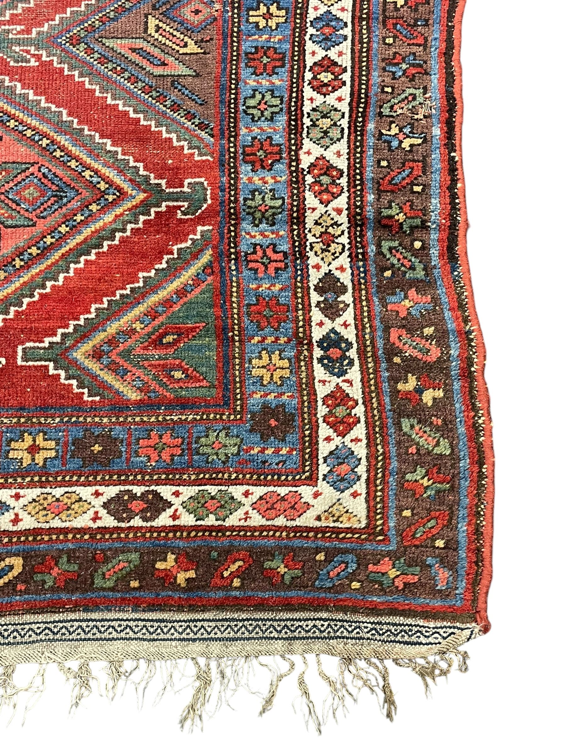 Kurdish crimson ground rug, the field decorated with four lozenge medallions, triple band border decorated with stylised flower heads