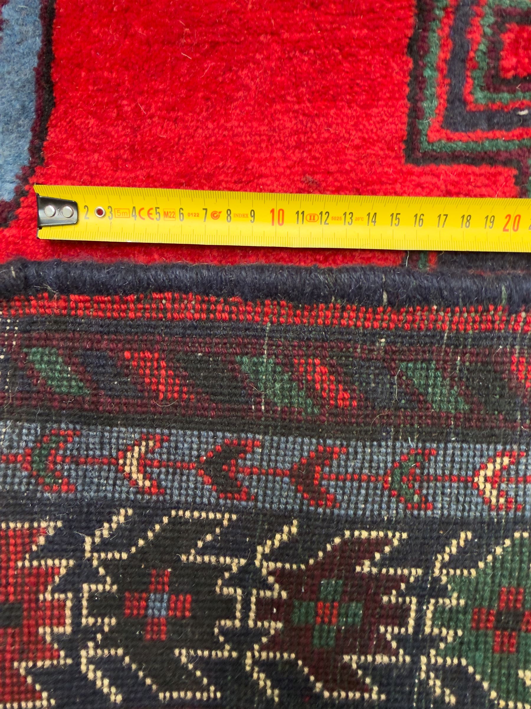 Northwestern Persian Cirjan hand-knotted carpet, madder red field with three linked stepped lozenge medallions in blue, ivory and green, flanked by angular motifs within a dark green border of serrated leaves and rosettes 