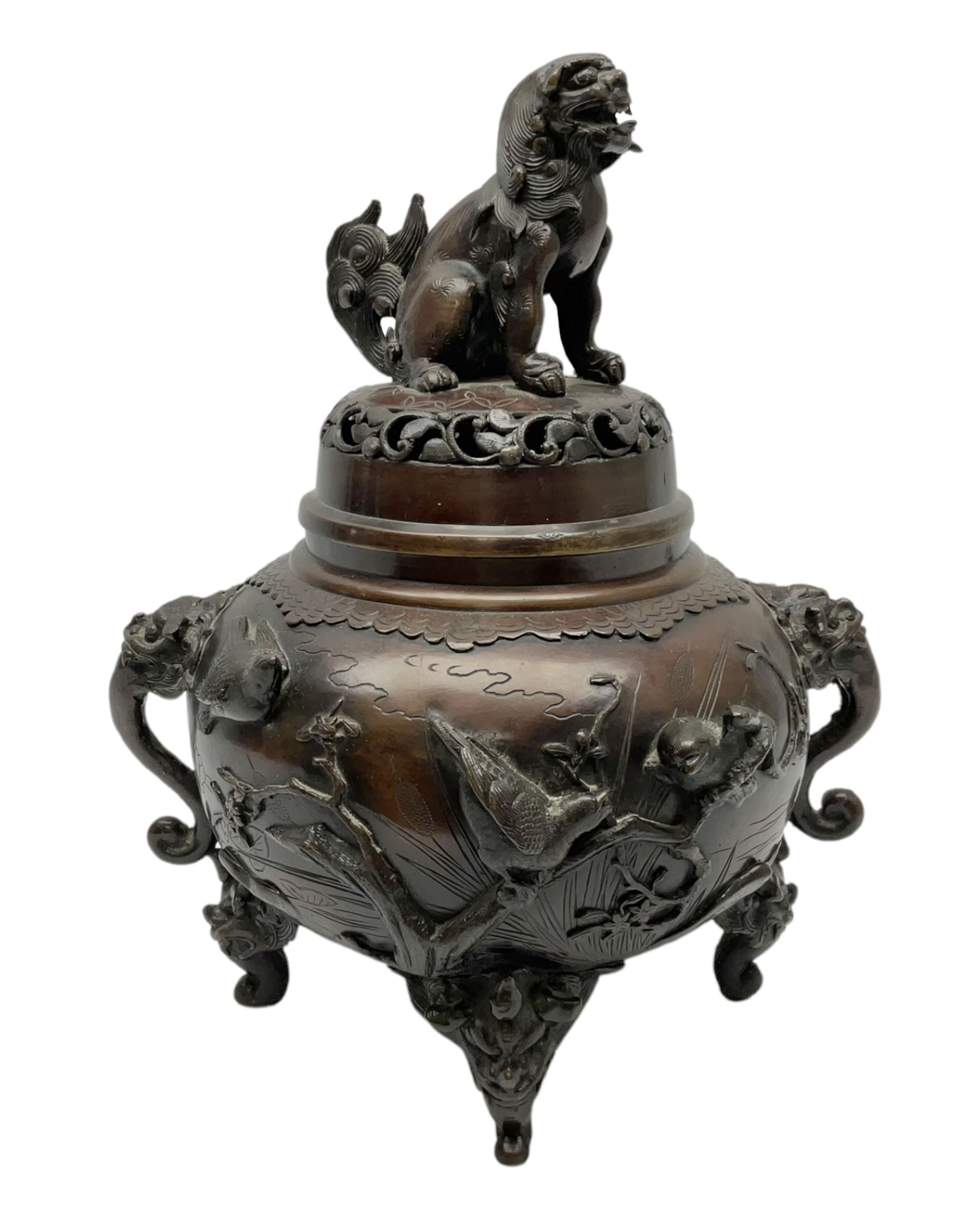 Japanese bronzed koro, the body of globular form with twin cast zoomorphic mask handles, decorated in relief with birds upon blossoming branches, against a ground incised with rushes and peonies, the flat toped domed cover with pierced band and surmounted by a cast figure of a Foo dog, the whole upon three zoomorphic mask feet, with impressed character type mark beneath, H35.5cm