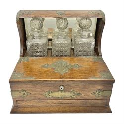 Edwardian oak tantalus with brass mounts and handles, the mirrored high-back with recess containing three square sided cut glass decanters, behind a hinged box, with cribbage board to the concealed drawer below, H32cm W35.5cm
