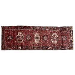 Persian Karajeh crimson ground runner rug, the field set with seven geometric lozenge medallions, the field decorated all over with stylised plant motifs, the banded border with repeating geometric shapes and patterns