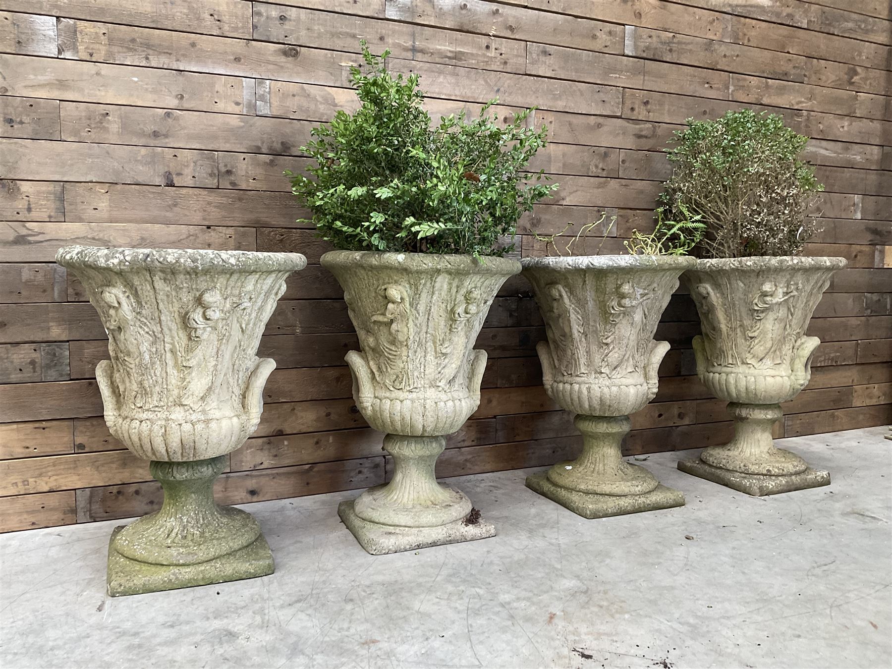 Set of four Victorian design cast stone Grecian urns, tapering form cast with figures and handles, square plinth bases