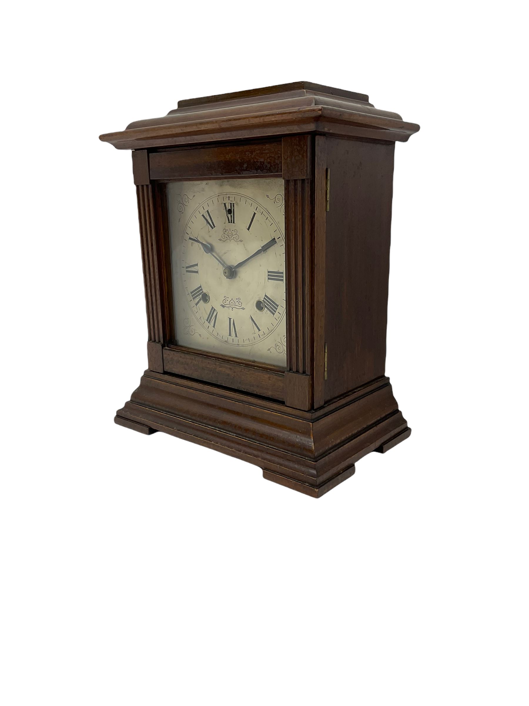 An American Mantle clock in a mahogany case with an eight-day “Ansonia” striking movement, case with a flat top and reeded pillars on a broad plinth with raised feet, square engraved and silvered dial with roman numerals and minute track, steel spade hands and pendulum regulation, sounding the hours and half hours on a coiled gong. With pendulum and key.  





