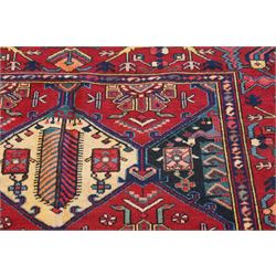 North West Persian Heriz hand-knotted rug, madder red field with an all-over lattice of stepped lozenge medallions enclosing stylized geometric floral motifs and ivory reserve panels, framed by angular vinery and motif borders, main border with with stylized rosettes and geometric devices, flanked by narrow guard stripes,, cotton fringe ends 