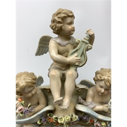  A late 19th century Sitzendorf porcelain mirror, the mirror plate of circular form set within a shaped surround encrusted with flowers and foliage, surmounted by three figures of cherubs and raised upon four scroll feet, with blue cross hatch mark beneath, H57cm.   