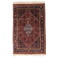 Persian crimson ground rug, central light blue lozenge medallion with floral motifs, the densely decorated crimson field filled with repeating flower heads and trailing leafy vines, the black and red border with interlacing foliate patterns and floral cartouches, surrounded by guard stripes