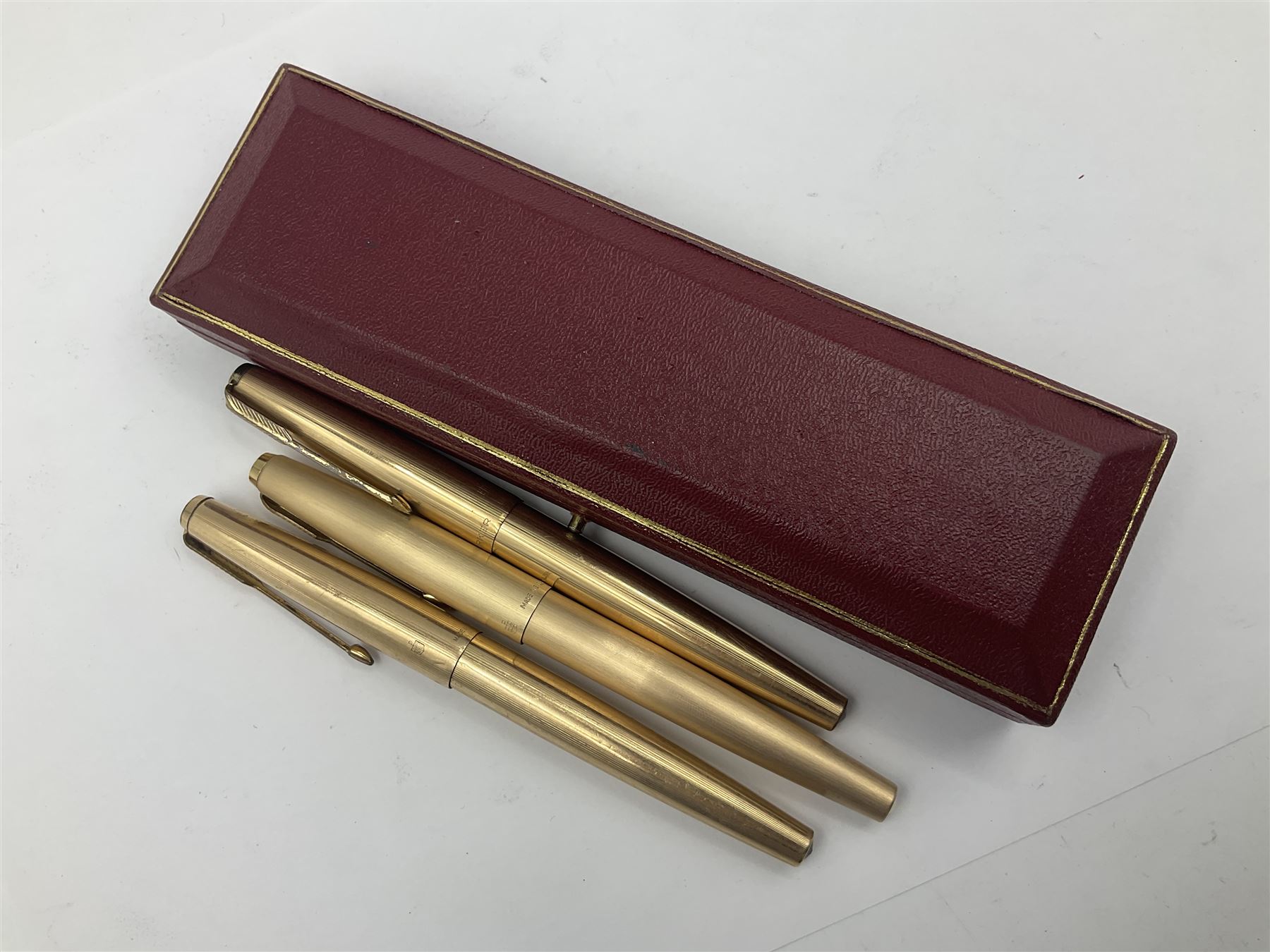 Three rolled gold Parker fountain pens, comprising an example with a gold nib marked 14K 585 and barrel with a shell stamp, a Parker 61 fountain pen with inset gold arrow to the nib, and another similar, all with striated decoration and arrow clips to the caps, L13cm, one with box
