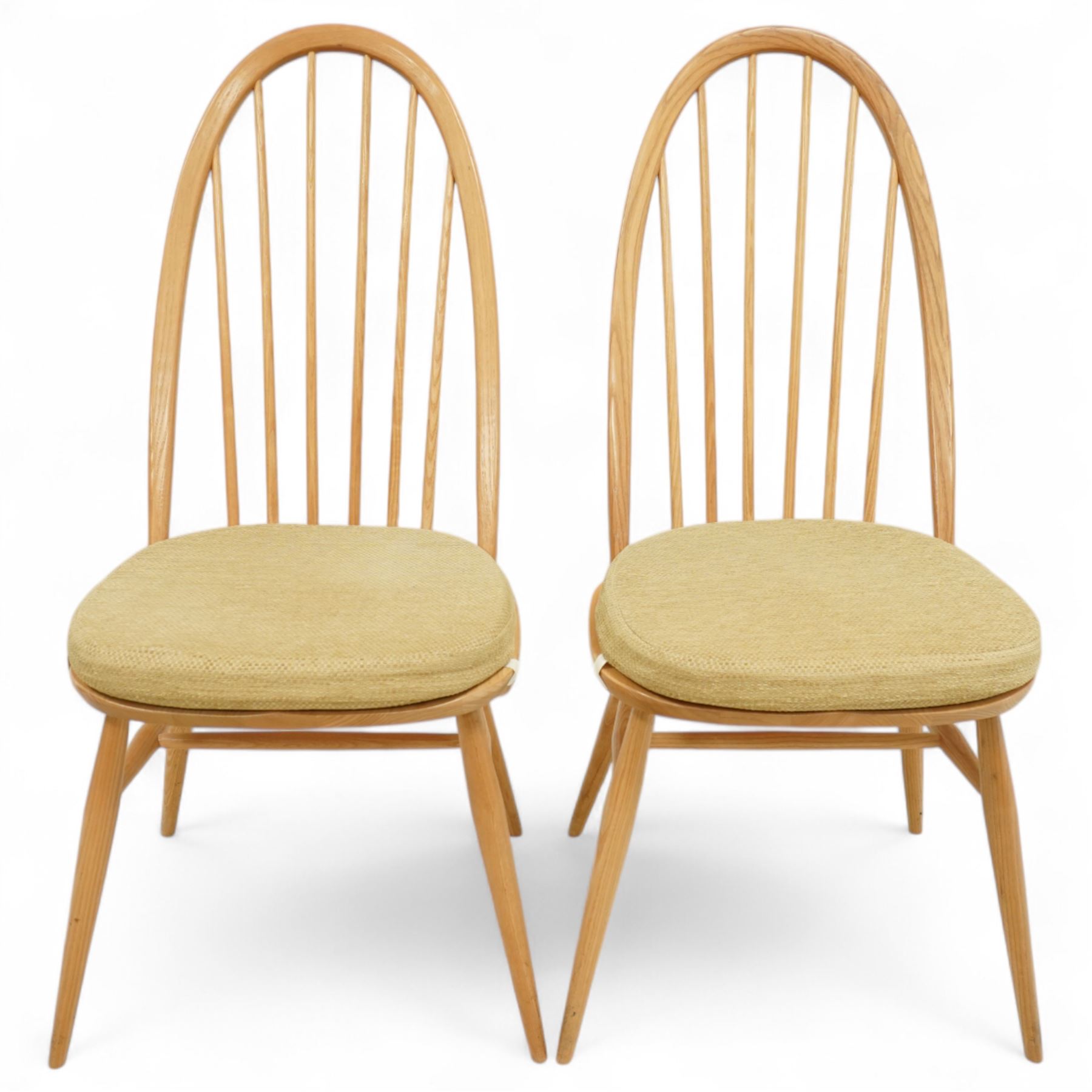 Ercol - light elm set of four Quaker style chairs, high arched backrest with slender spindles, solid wood seat with elasticated strap cushion, on round tapered out swept legs (4)