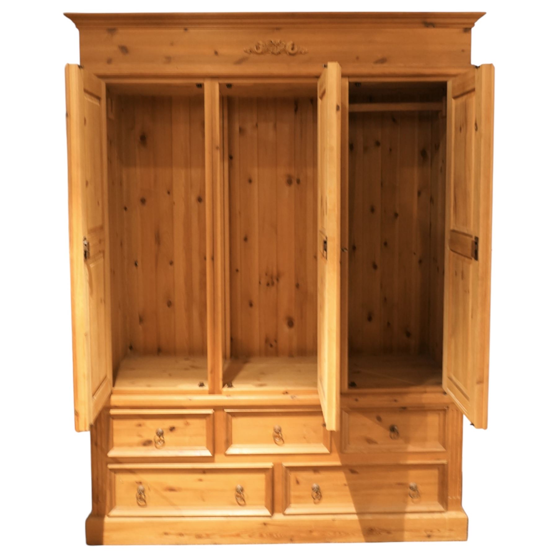 20th century pine wardrobe with drawer base, moulded cornice over three fielded panel cupboard doors enclosing hanging compartments, the base fitted with three short and two long drawers with brass ring handles, raised on a plinth base