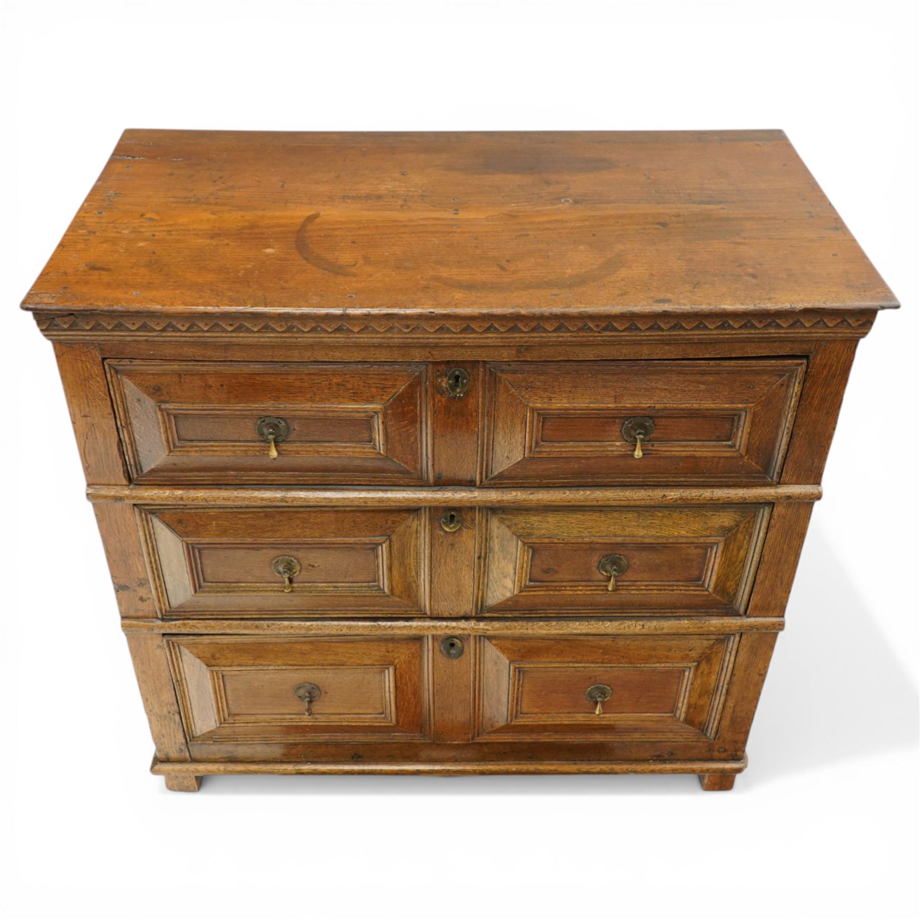 18th century oak chest of drawers, rectangular plank top with chip carved frieze, fitted with three long geometrically panelled drawers with applied mouldings, later brass drop handles, on stile supports, panelled sides and boarded back