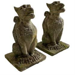 Pair of weathered cast stone grotesque garden figures, in the form of winged beasts with chained claws, on square plinth base
