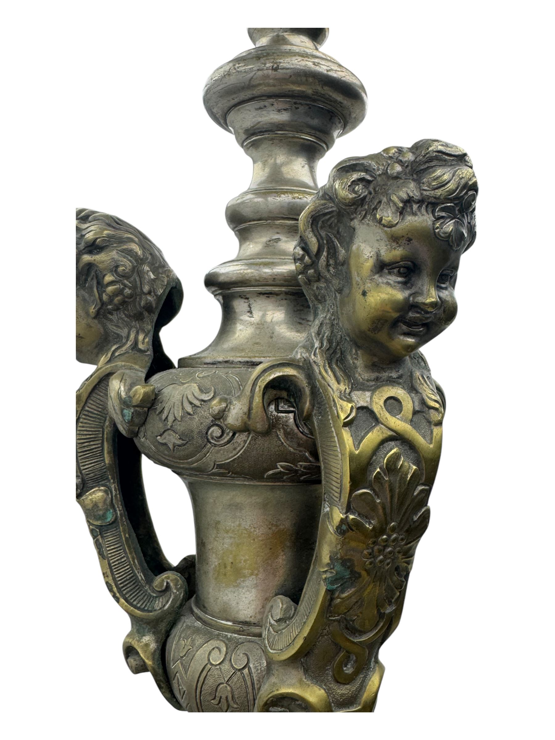 Early 20th century cast brass chandelier, the main baluster-form body surmounted by a lobed finial, with three cherubic heads and foliate scrollwork around the upper section, eight sweeping branches for lights