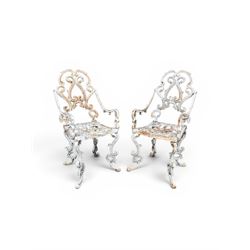 Pair of Victorian cast iron garden chairs, the ornate pierced back of scrolling foliate design, scrolling arm terminals over splayed supports formed of C and S-scrolls, in distressed white painted finish