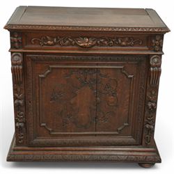 19th-century heavily carved oak baroque style cupboard with vine and floral carved frieze drawer above panelled cupboard door with floral carved appliqué (detached) flanked by symmetrically carved scroll and vine decorated sides, on bun feet 