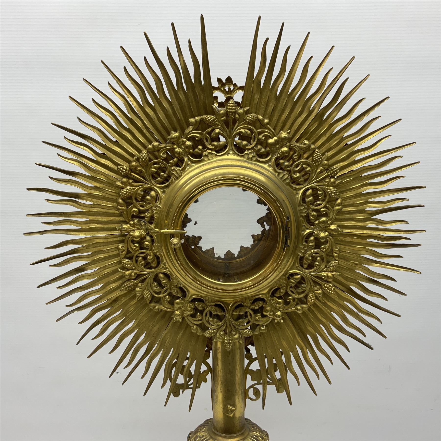 20th century gilt metal monstrance, in the Gothic revival style, with glazed aperture to centre surrounded with clear paste stones, in a pierced floral and scroll border set with coloured paste stones, within a sunburst surround, on a paste set knopped stem and similar foliate foot, H59.3cm