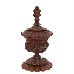 Carved wooden urn. decorated in relief with carved faces within foliage, with a Satyr finial, H25cm 