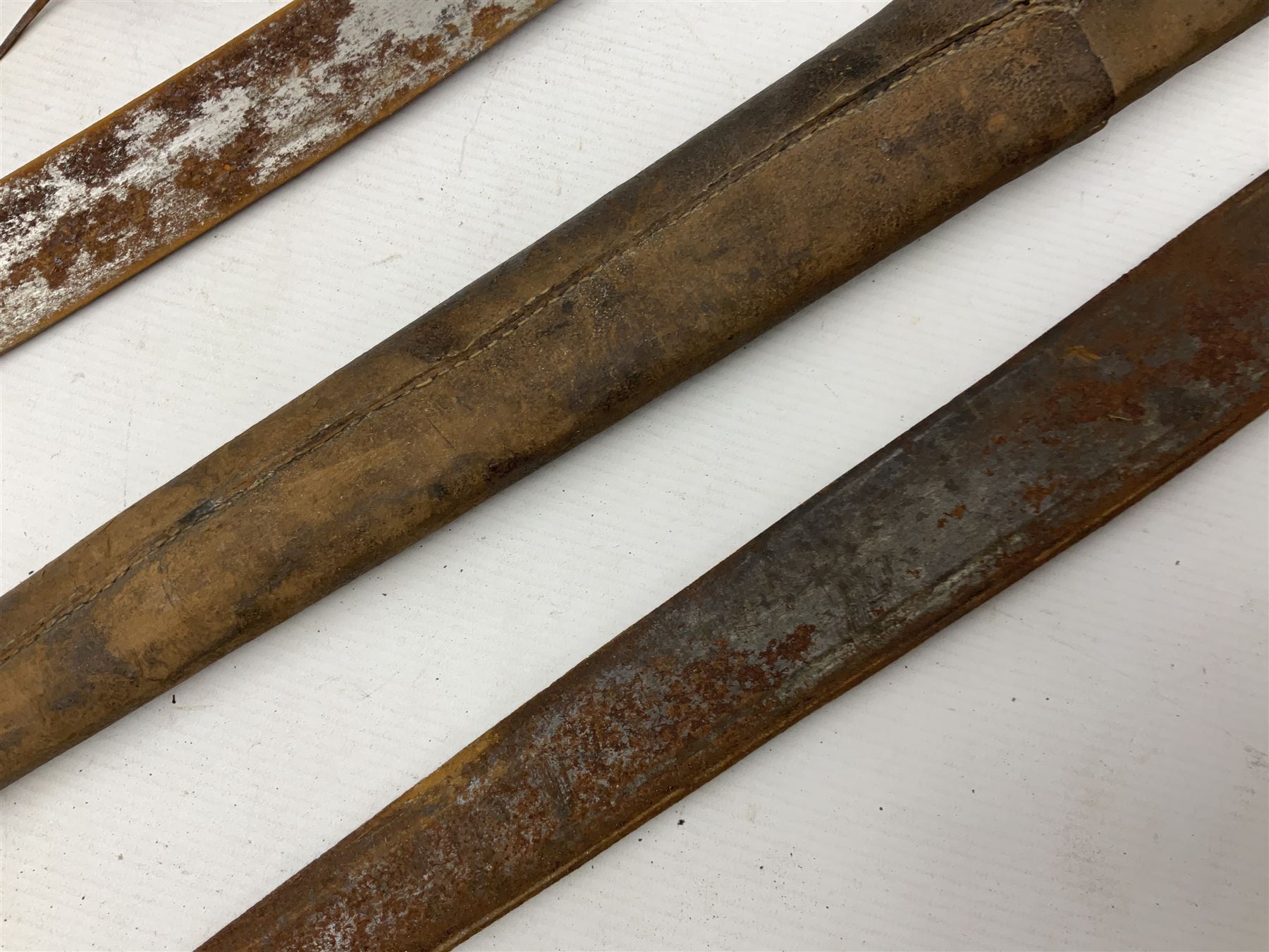 Mandingo sword, the 63cm plain curving steel blade marked with a horses head and the initials G.S.; leather covered grip with metal ribbed spherical pommel; in decorative leather leaf scabbard mounted with tassels and roundels L84cm overall; and a North African flyssa sword in poor condition with wooden scabbard (2)
