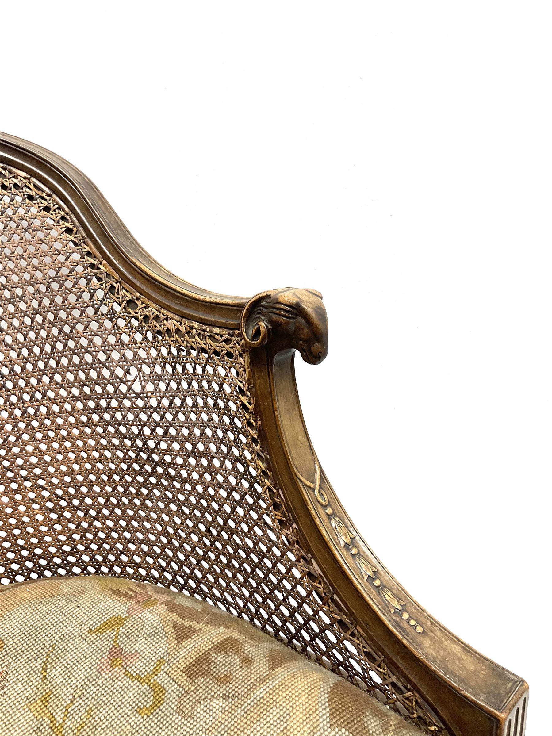 Early 20th century walnut Bergère chair, moulded and shaped frame terminating in rams head, cane woven back meets patterned upholstered seat, raised on leaf carved and fluted supports 