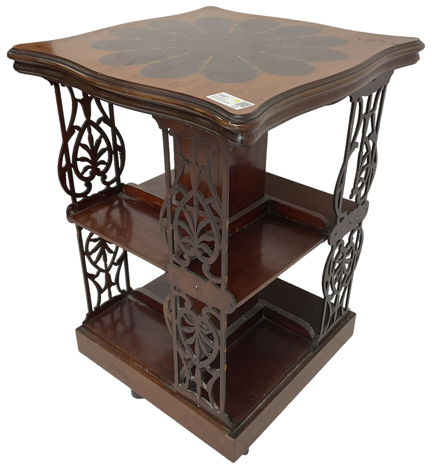 Edwardian mahogany revolving bookcase, the shaped moulded top inlaid with cusped panel and trailing bellflowers within a satinwood frame, foliate pierced upright splats and central square column supporting two tiers, on cruciform base with brass and ceramic castors 