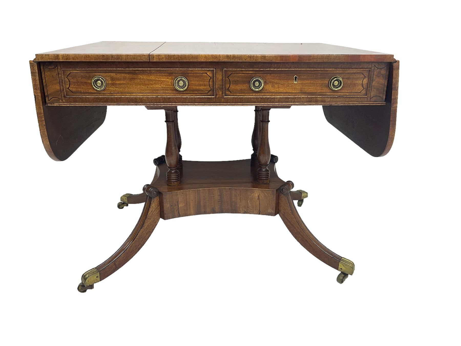 Regency period mahogany drop-leaf sofa table, rectangular top fitted with two cockbeaded drawers with ebony stringing, raised on turned columns united by quadrupod base, the sabre supports terminating in brass cups and castors