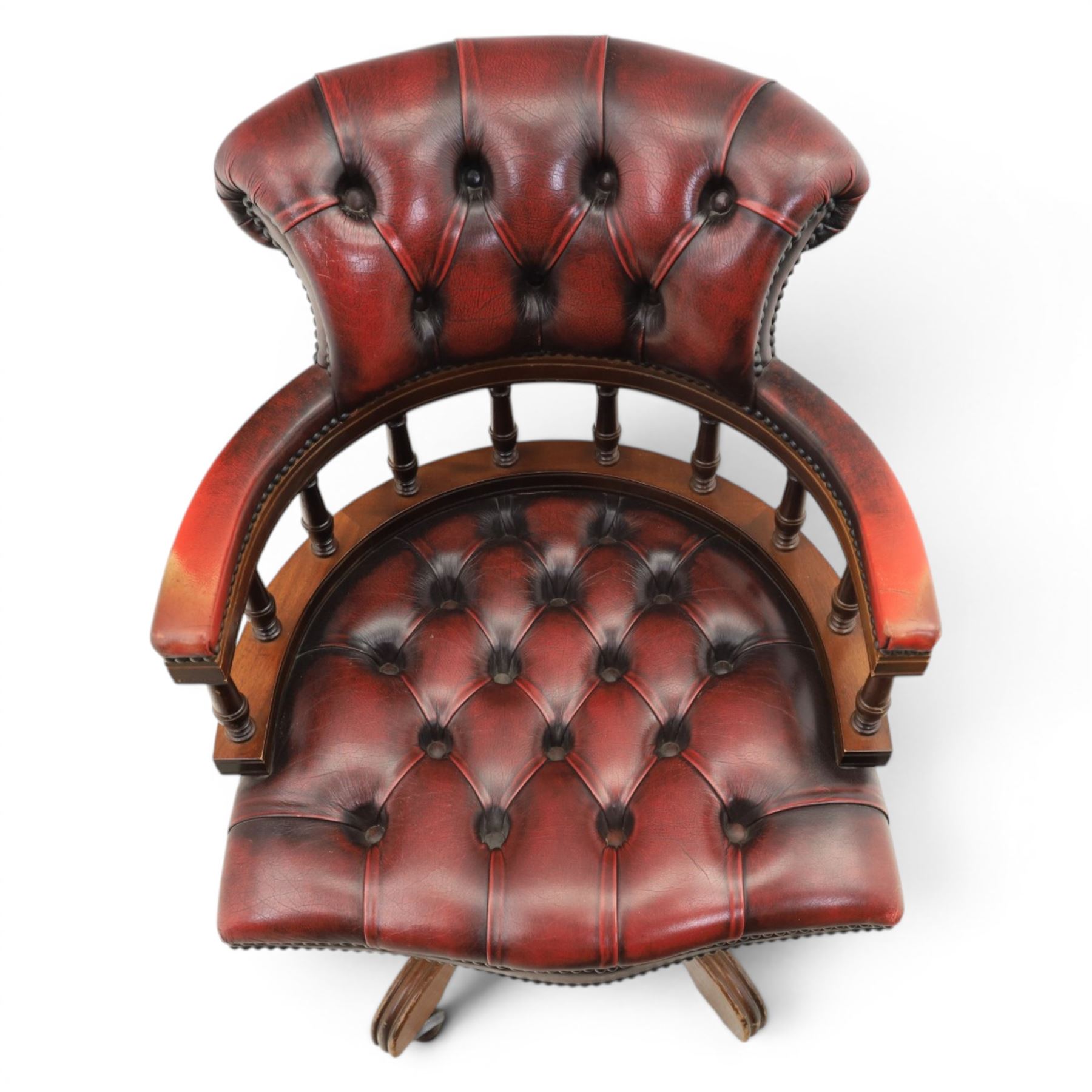 Captains swivel desk chair upholstered in oxblood leather, buttoned back and seat, shaped arm bow raised on turned spindles, five spoke base raised on castors