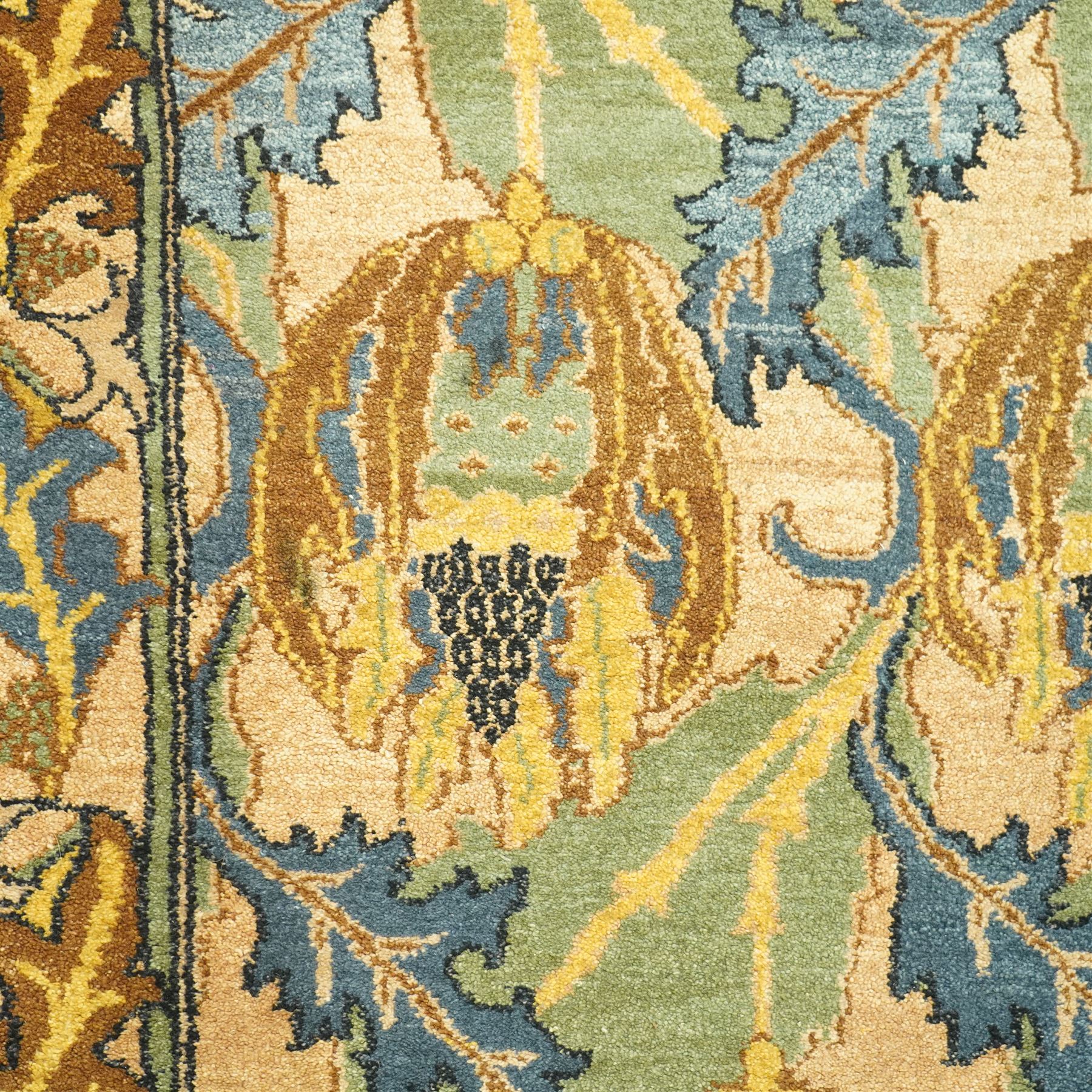 Arts & Crafts design wool pile rug, decorated with repeating stylized floral seed-head motifs and scrolling foliage within a complementary floral border in a muted palette of green, ochre, blue, and brown, with cotton fringe ends, with label for London House Oriental Rugs & Carpets  