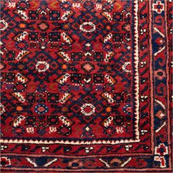 North West Persian Malayer hand-knotted runner, decorated with a dense all-over pattern of small repeating boteh and rosette motifs on a rich madder red ground, field filled with geometric floral elements arranged in a lattice design, framed by a narrow main border and flanked by slender guard borders, with cotton fringe ends 