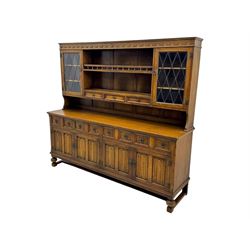 Large mid-20th-century oak dresser with two astragal glazed doors between gallery shelf and lower shelf, with three short drawers and lower section with four drawers and three double-panelled linen-fold hinged cupboard doors 