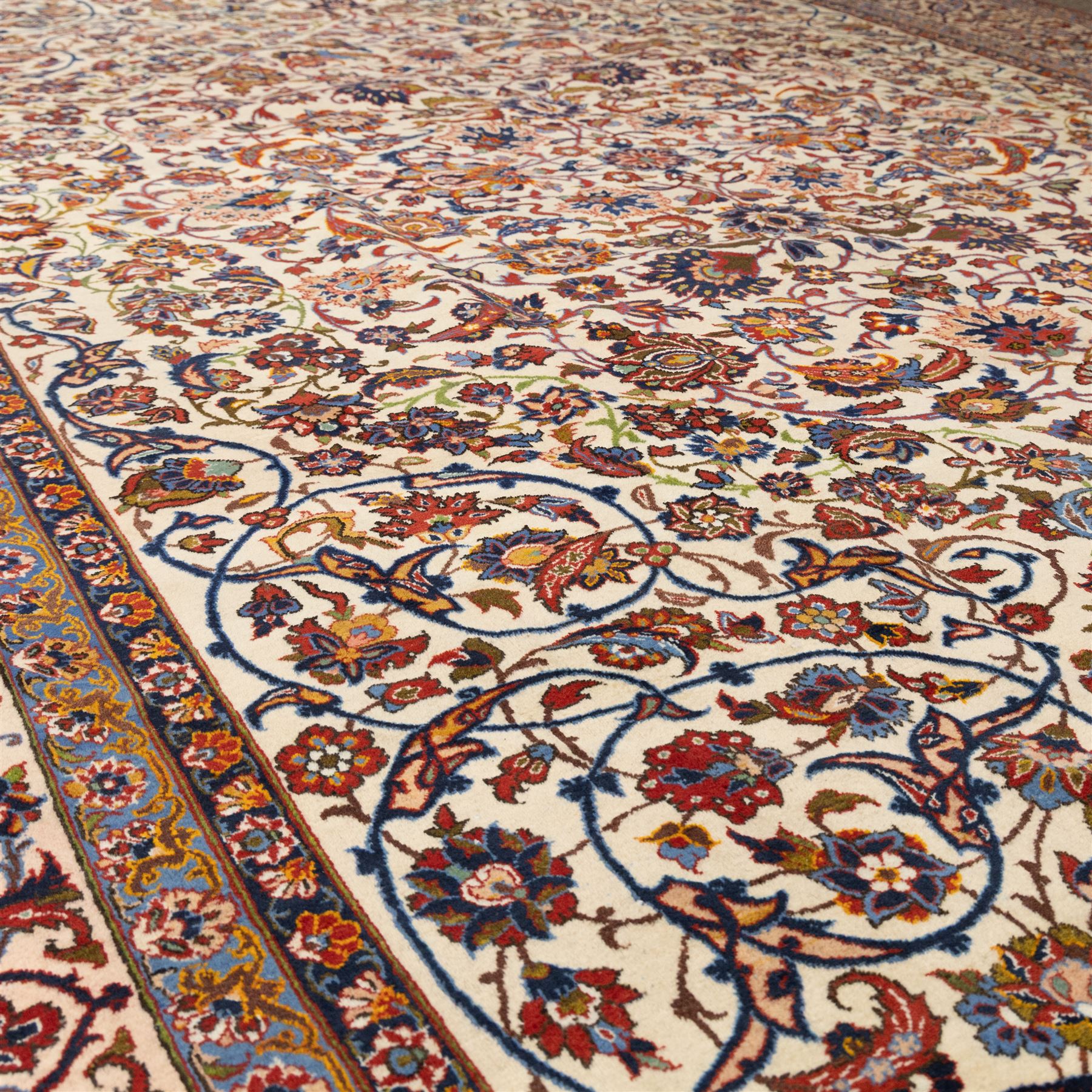 Central Persian Najafabad hand-knotted carpet, ivory field with an all-over scrolling floral design of palmettes, rosettes, and leafy vine work, enclosed by a wide floral main border flanked by multiple guard borders in madder red, indigo blue, green, and pale ochre, with cotton fringe ends 