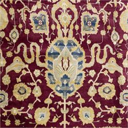 Agra design wool carpet, burgundy field decorated with large scrolling floral vines, palmettes and flowerheads, enclosed by blue main border with oversized stylised palmettes and narrow guard stripes