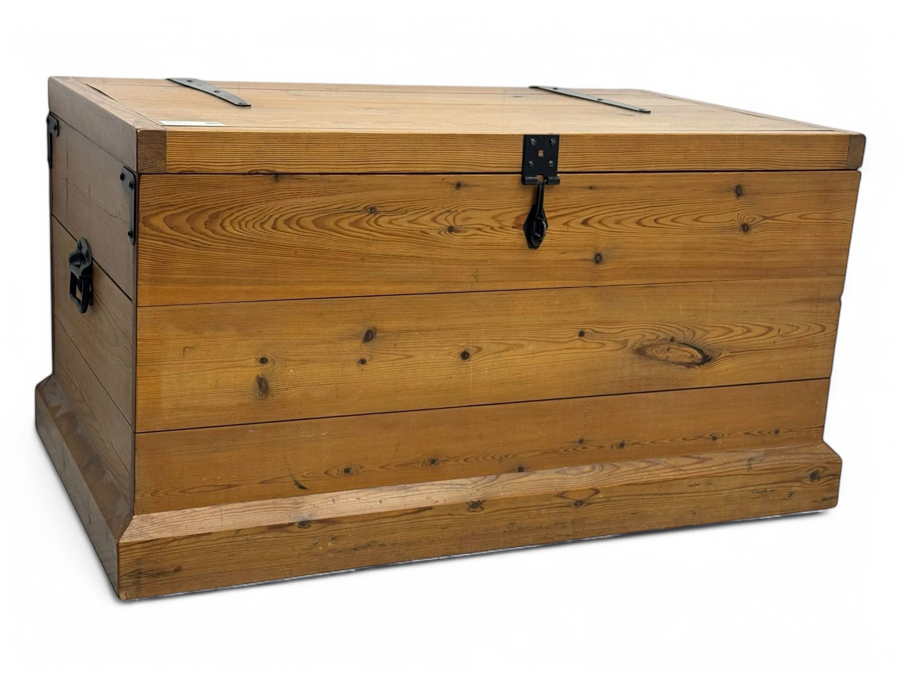 Contemporary polished pine blanket chest, the hinged planked lid with iron strap hinges and clasp fitting, plain boarded sides, fitted with blackened metal drop handles, on a moulded plinth base