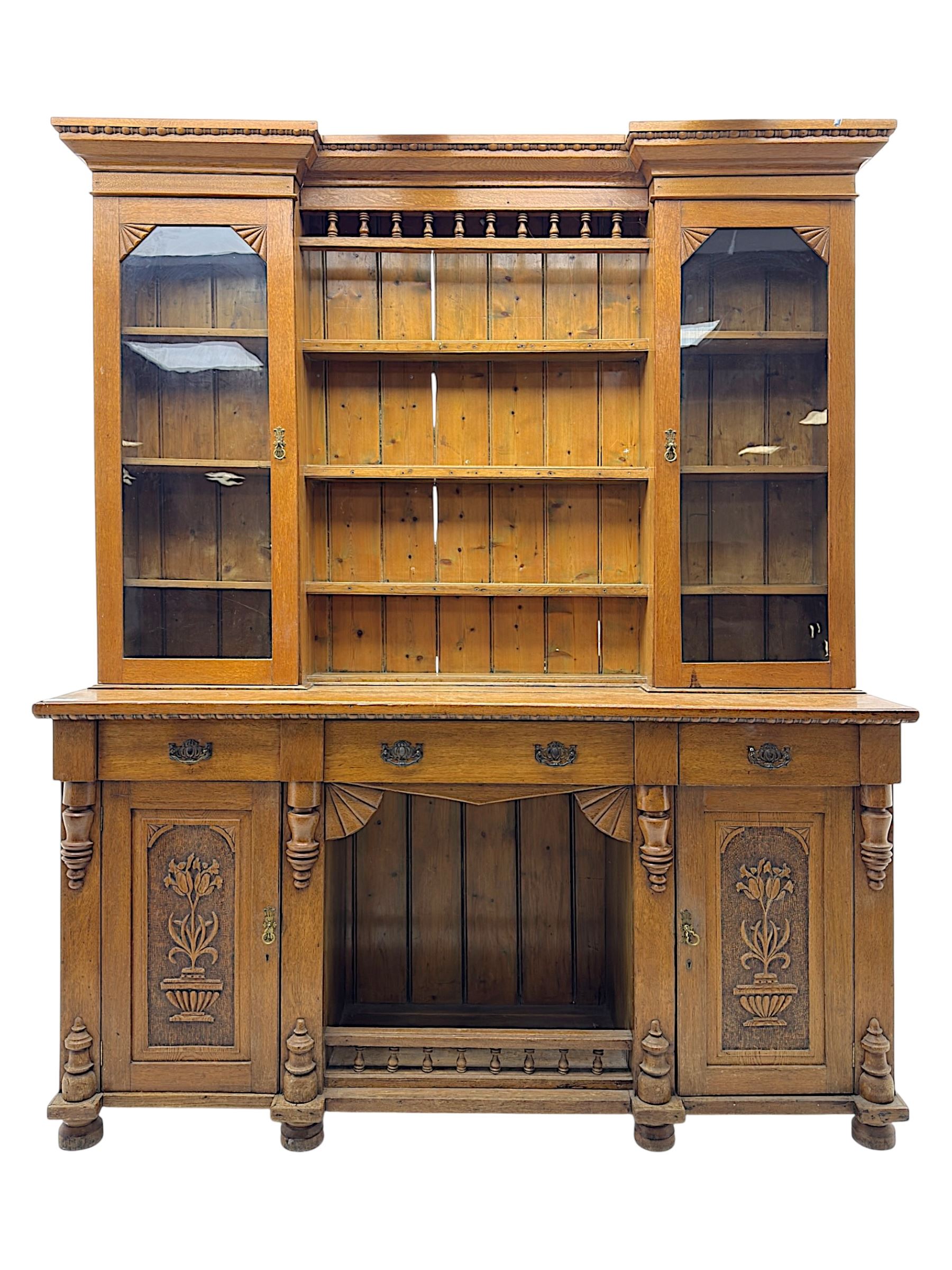 Late 19th century pine dresser, the projecting cornice with dentil and spindle moulded frieze above a three-tier plate shelves, flanked by glazed doors, the base fitted with three frieze drawers over arched apron and carved floral panelled cupboard doors, raised on turned feet