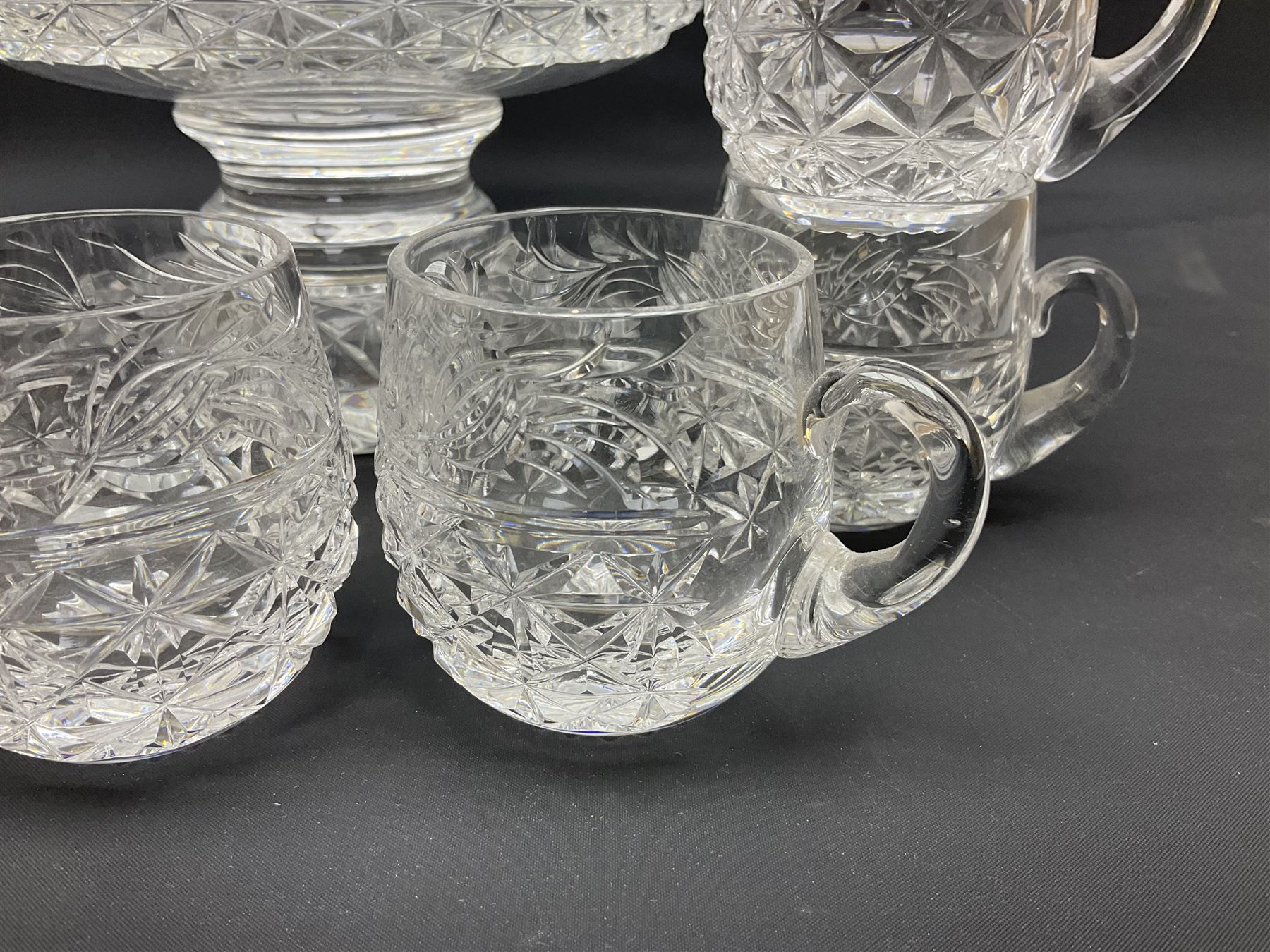 Large Stuart crystal pedestal punch bowl, of circular form, the rim with engraved floral decoration, upon spreading circular foot with radial cut decoration, with seven matching Stuart crystal drinking glasses, each with a C handle, each acid signed beneath, bowl H20cm