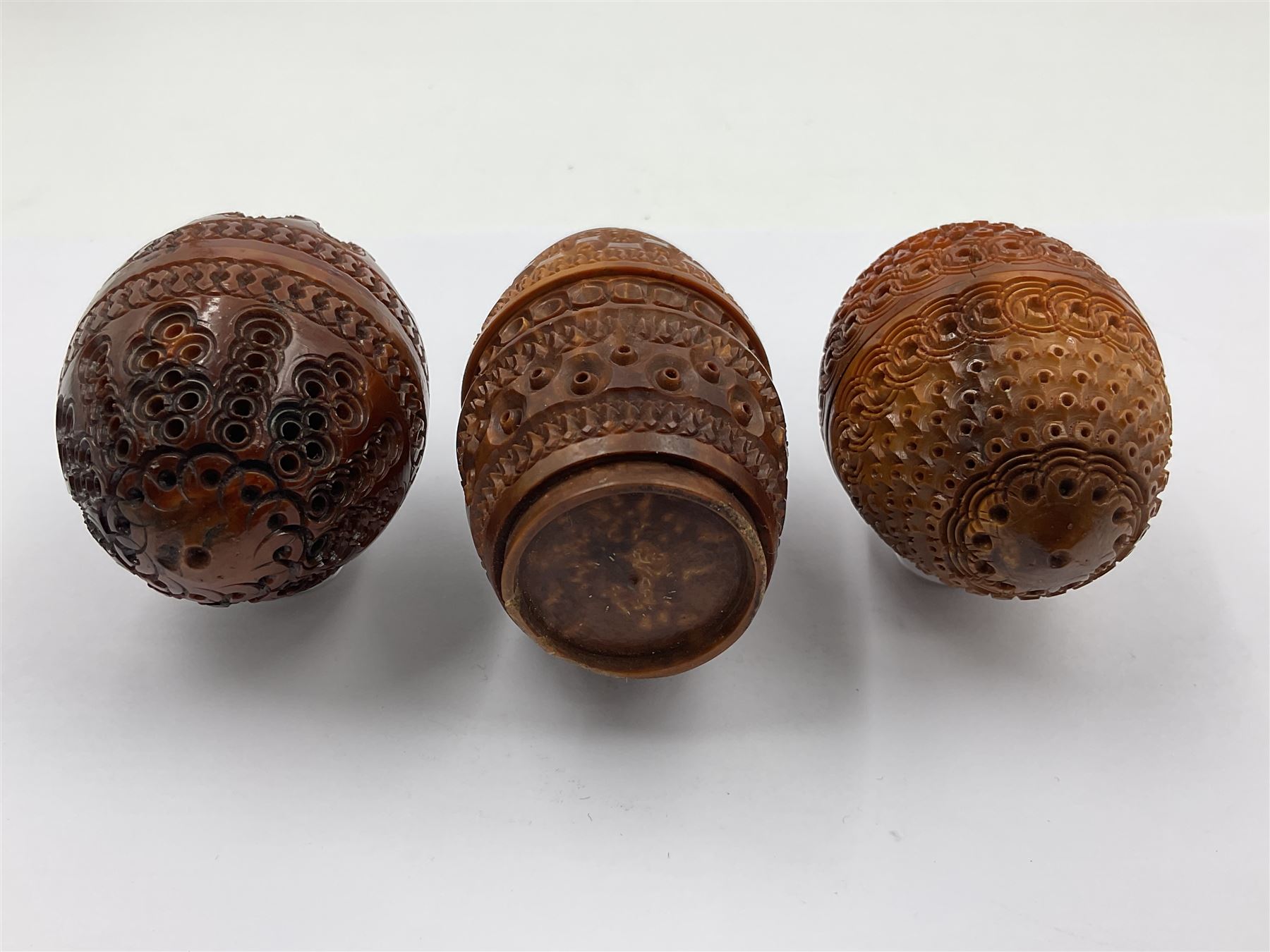 Three 19th century coquilla nut pomanders or flea catchers, two of egg shaped form and the third of barrel from with carved and pierced decoration and screw threaded join, largest H8cm