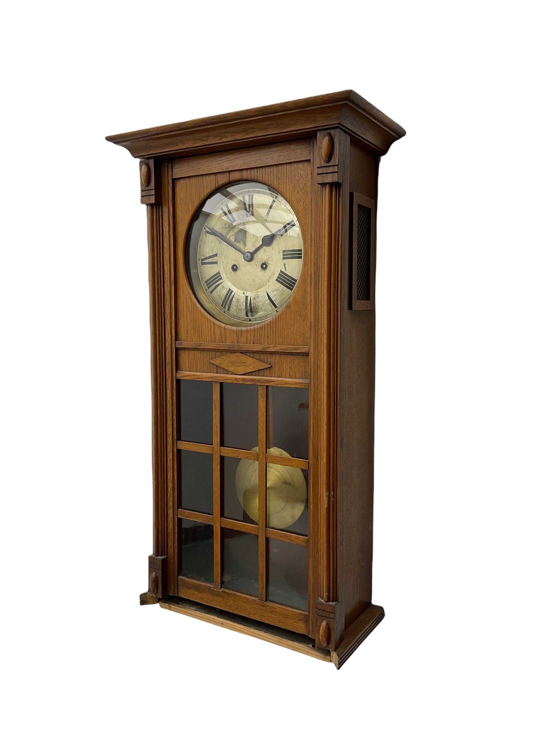 A 1930’s German eight-day spring driven wall clock by Philipp Hass & Sohne striking the hours and half hours on a gong, with an eight-inch silvered dial with a spun brass bezel, Arabic numerals, minute track and steel spade hands, in a flat-topped oak case with full length door and applied mouldings, nine glazed panels with a visible spun brass pendulum. With key.                                   