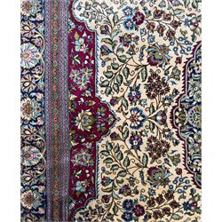 Central Persian Ghom hand-knotted rug, ivory field with scrolling vines, palmettes and flowerheads around a central lobbed medallion with pendants, framed by burgundy spandrels and a navy border of rosettes and arabesques, 289cm x 214cm