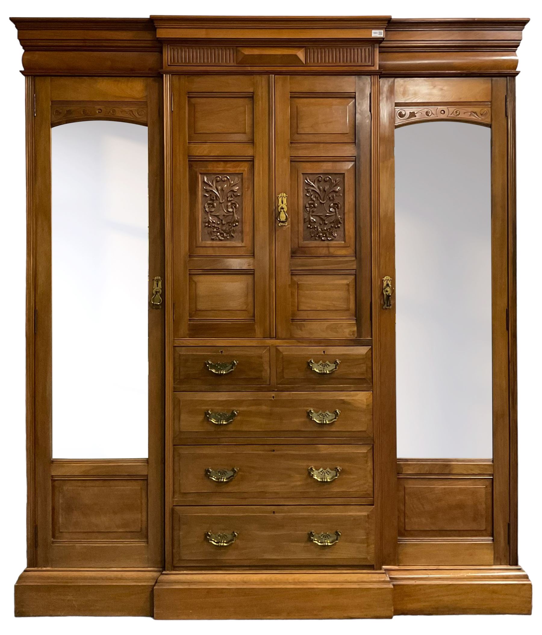 Edwardian walnut combination breakfront triple wardrobe, projecting cornice over cushioned and fluted frieze, central fielded panelled cupboard carved with foliate decoration above two short and three long drawers, flanked by two bevelled mirror doors enclosing hanging hooks with single drawers to base, retailed by J Tonks & Sons, Scarborough