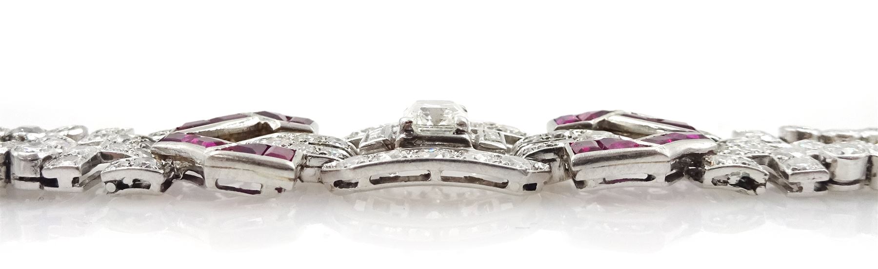Art Deco platinum diamond and ruby bracelet, circa 1920-1930, the central panel set with a single emerald cut diamond of approx 0.55 carat, flanked by two baguette cut diamonds and old cut diamond surround, the articulated geometric design bracelet with vari-cut rubies, round and baguette cut diamonds, total diamond weight approx 7.00 carat, in Mappin & Webb silk and velvet lined box