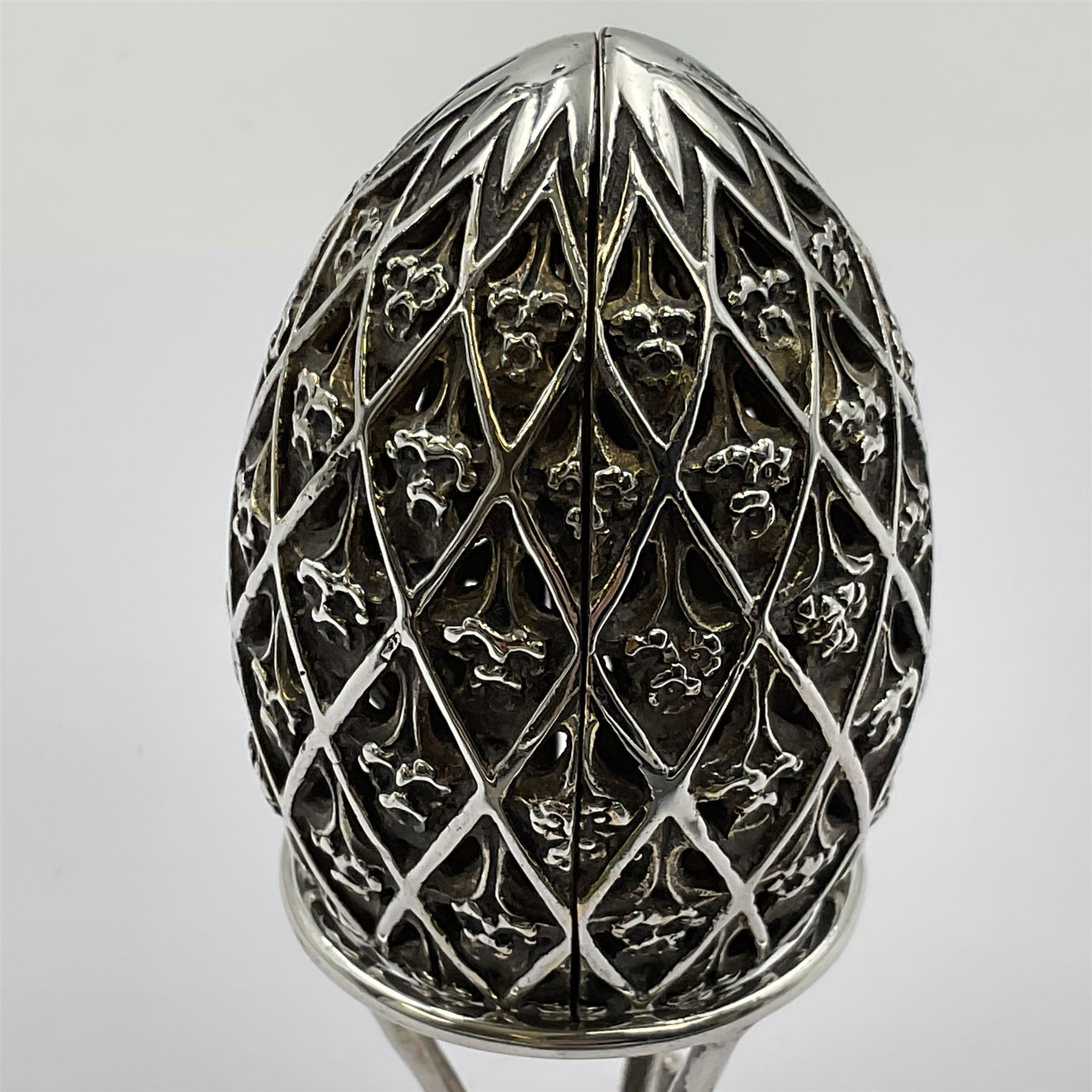 Modern silver limited edition Easter egg, no. 70/500, the openwork lattice body decorated with gilded panels of flower heads, opening to reveal a gilt interior, upon silver stand with three scrolling pad feet, each hallmarked St James House Company, London 1979, height including stand 8cm
