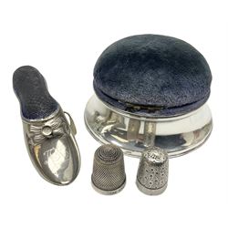 Silver mounted pin cushion, of circular form, together with two silver thimbles, and a base metal pin cushion with tape measure, modelled in the form of a shoe 